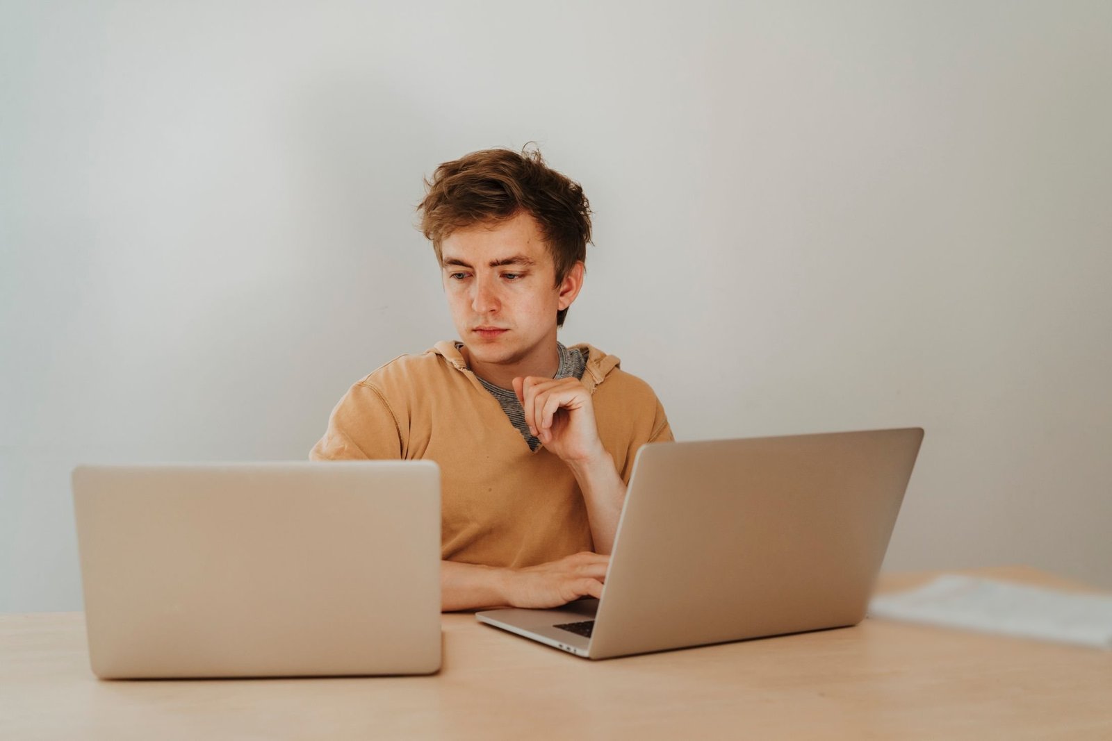 A developer rests their chin on one hand while comparing two laptops on a plain desk