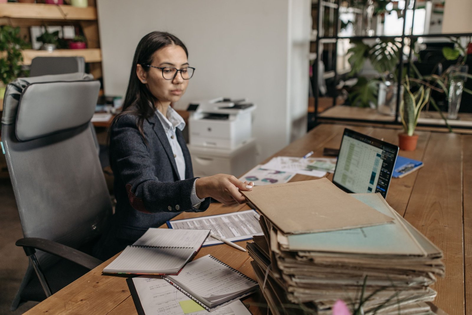 Office worker at a desk with stacked case folders and a laptop showing a spreadsheet
