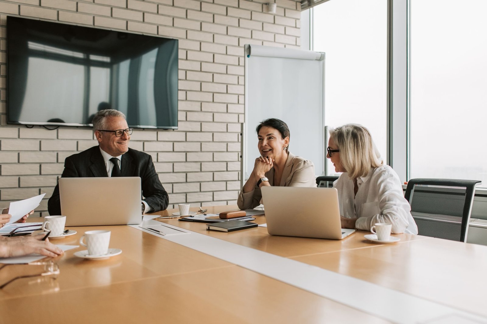 Three colleagues with laptops talk around a meeting table in a bright conference room